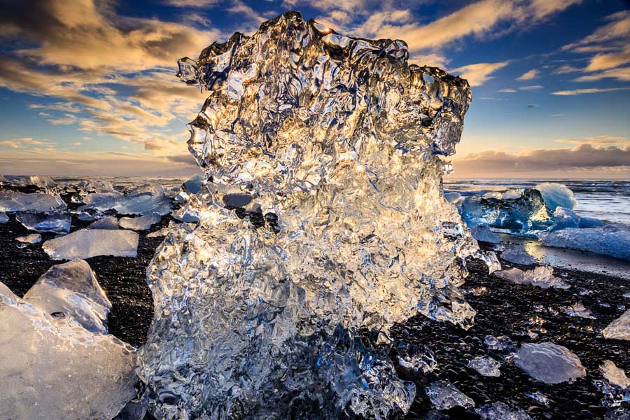 The morning sun is shining through a growler on the black pebble beach at Jökulssarlon