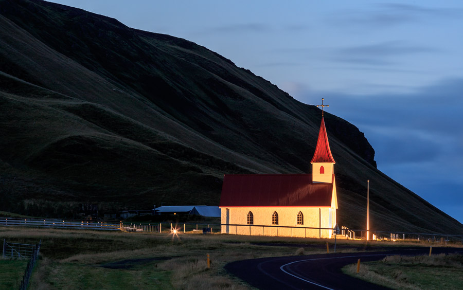 Reyniskirkja lit up at night against the obligatory mountain backdrop